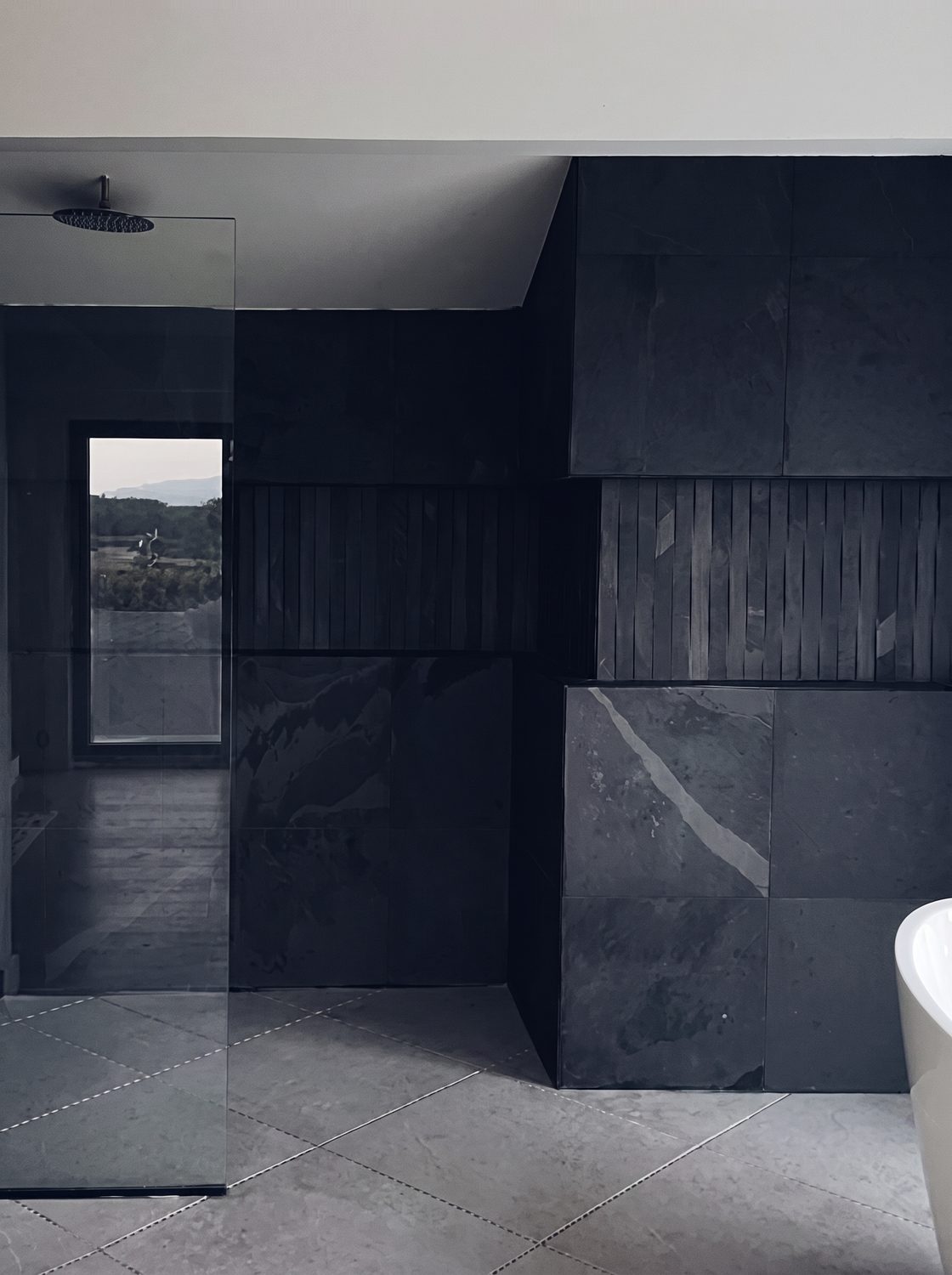 Slate tiled walk in shower beside a freestanding tub