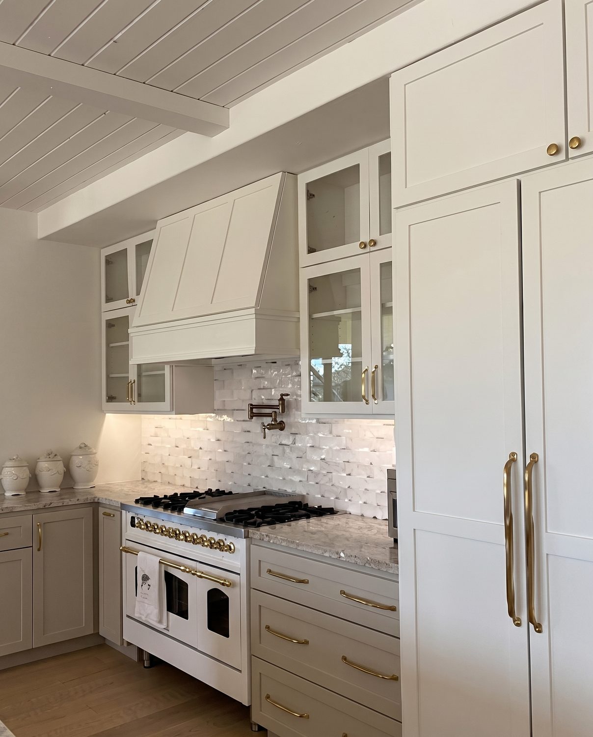 Cream kitchen with a plaster range hood, brass hardware and an integrated refrigerator